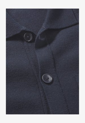 Marineblauwe gebreide polo met een gladde textuur, voorzien van een kraag en twee zwarte knopen aan de voorkant.