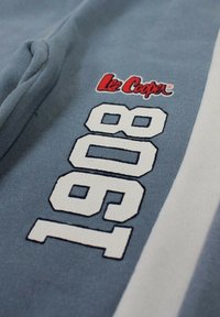 Tissu bleu avec le logo "Lee Cooper" en rouge et blanc, et de grands chiffres blancs "1989" imprimés verticalement à côté d'une bande claire.