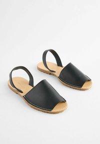 Sorte læder slingback sandaler med åben tå. Struktureret overflade, kontrasterende hvid syning og en naturlig korksål.