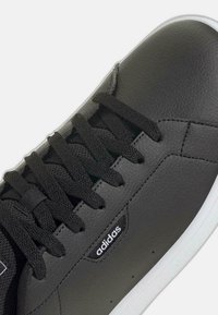 Czarne sneakersy Adidas z teksturowaną skórzaną cholewką, czarnymi sznurówkami i białą podeszwą, ukazujące zbliżenie na bok i czubek.