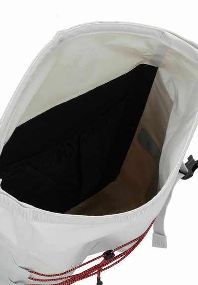 Sac blanc avec un extérieur texturé, présentant une poche intérieure noire, un cordon de serrage rouge et une forme lisse et non structurée.