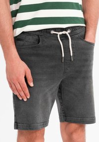 Shorts en denim gris foncé avec taille à cordon, poches avant et légère elasticité. Texture lisse, bords ourlés et design décontracté.