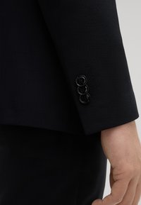 Donkerblauwe blazer manchette met een gladde textuur, drie zwarte knopen aan de achterkant en subtiele stiksels.