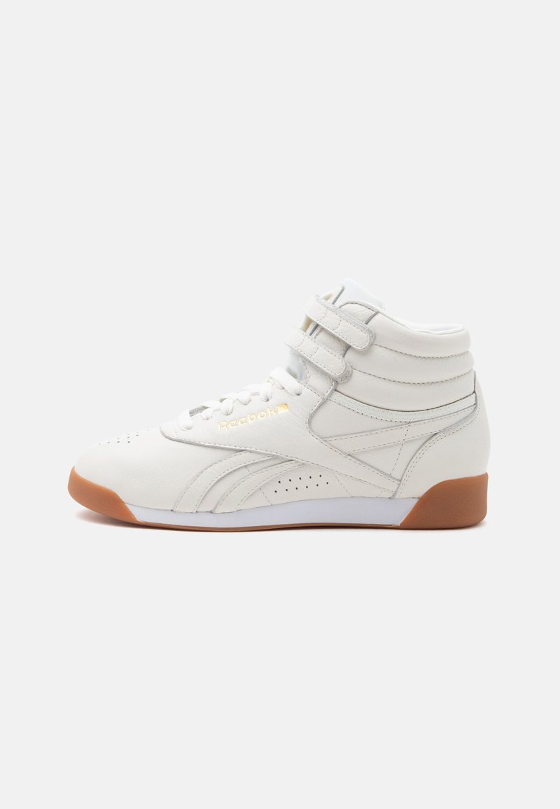 Baskets montantes blanches Reebok avec doubles sangles à la cheville et semelle en gomme, vues de côté sur un fond uni.