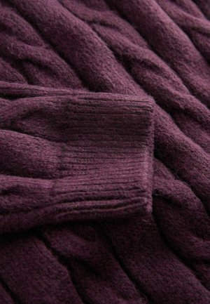 Strickpullover aus tiefviolettem Wollgarn mit einem strukturierten Zopfmuster und gerippten Bündchen, der ein weiches und voluminöses Erscheinungsbild zeigt.