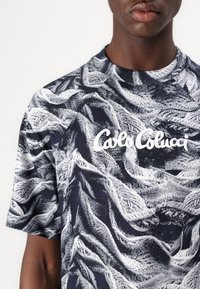 Short-sleeve T-shirt featuring a navy and white abstract pattern, round neck, and embroidered "Calo Colucci" logo on the front.