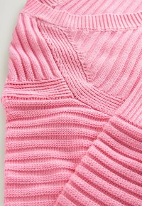 Närbild av en rosa stickad tröja som visar ribbade mönster och detaljerad sömnad på ärm och halsringning.