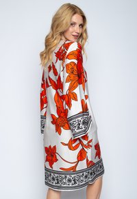 Kwiatowa sukienka z białym tłem, dużymi pomarańczowymi kwiatami oraz czarnymi, skomplikowanymi wzorami na rękawach i dolnej krawędzi, lekka, luźny krój.