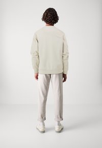 Felpa beige chiaro con scollatura girocollo classica, abbinata a pantaloni grigi chiari e sneakers bianche, caratterizzati da orli arrotolati e una vestibilità rilassata.