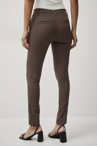 Bruine slim-fit broeken met een gladde textuur, voorzien van achterzakken en een mid-rise tailleband, gecombineerd met zwarte blokhak sandalen.