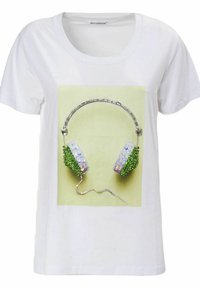 Camiseta blanca con un gráfico de auriculares adornados con acentos de joyas verdes y claras, contra un fondo amarillo pálido.