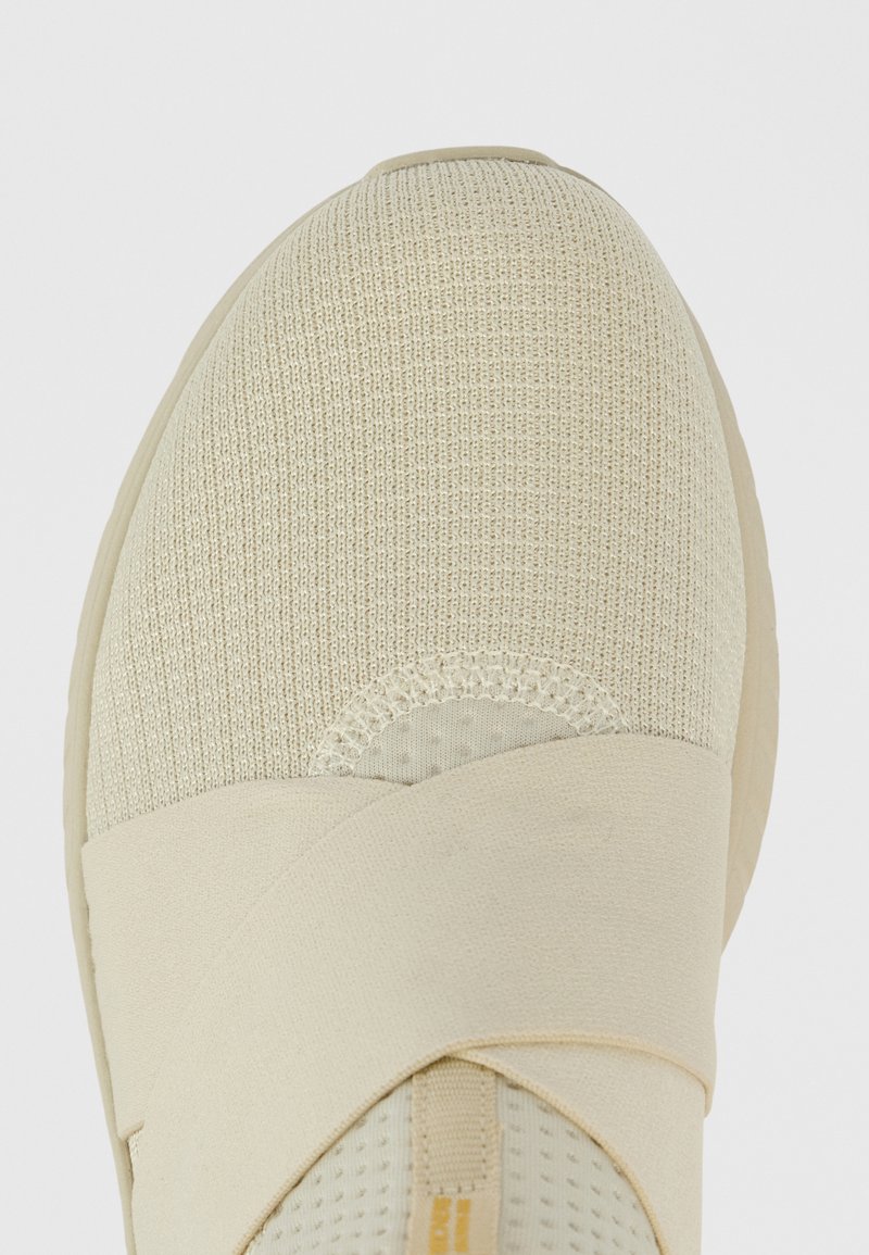 Zapatillas deportivas beige con un upper texturizado, correas elásticas cruzadas y un diseño de punta redondeada con un panel de malla para mayor transpirabilidad.