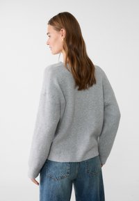 Grauer gestrickter Pullover mit bequemer Passform. Mit gerippter Textur, überschnittenen Schultern und einem leicht verkürzten Saum. Dazu kombiniert werden blaue Jeans.