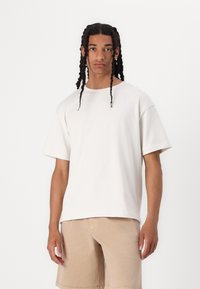 Lichtbeige katoenen t-shirt met een ronde hals en korte mouwen, met een ontspannen pasvorm en een zachte textuur. Draagt met beige shorts.