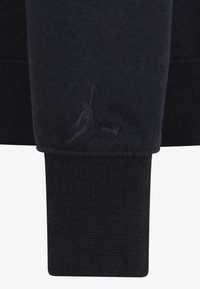 Manche de sweat-shirt noire avec un logo Jumpman brodé en relief près du poignet côtelé.