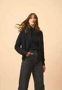 Mustat neulejakut päällä musta poolopaita, yhdistettynä korkeavyötäröisiin tummaan farkkuihin. Tekstuuri on sileä, mukautuva istuvuus ja avoin etuosa.