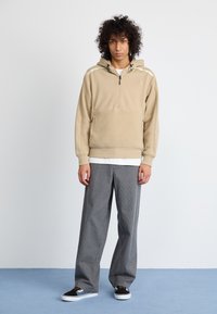 Sudadera de forro polar beige con un diseño de media cremallera y bolsillo tipo canguro, combinada con pantalones de pierna ancha de rayas grises y zapatillas negras.