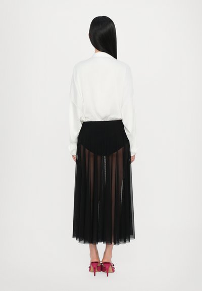 White oversized shirt paired with a black sheer pleated skirt and pink high-heeled shoes, showing layered textures and contrasting colors.