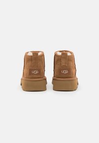 Botines de ante marrón con interior suave, puntera redondeada y suela de goma. Logo de UGG en la parte trasera, con una cinta de tirón para facilitar el uso.