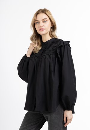 Blusa nera a maniche lunghe con maniche a sbuffo, dettagli arricciati sulle spalle e frontale plissettato. Il tessuto appare morbido e leggero.