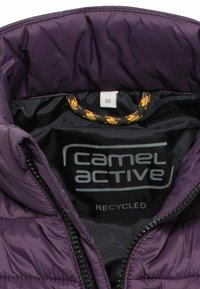 Purpurowy pikowany kołnierz kurtki z etykietą marki "camel active", metką rozmiaru 50 oraz żółto-czarną pętlą wewnątrz.