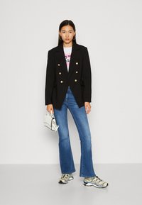 Musta kaksirivinen blazer, jossa on kultaiset napit, käytetty valkoisen t-paidan päällä, yhdistettynä pillifarkkuihin ja valkoisiin tennareihin.