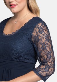 Modré námořnické šaty s krajkovým potiskem květin, výstřihem do V a rukávy tříčtvrteční délky. Hladká tkanina s sklady.