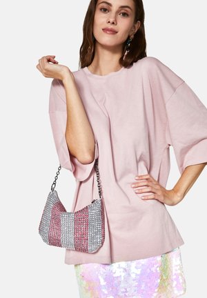 Perlebesat håndtaske i sølv, rød og pink nuancer, med en unik buet form og en kæderekke. Modellen har en blød pink oversized t-shirt på.