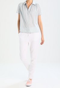 Chemise à manches courtes rayée, de couleur bleu clair, associée à un pantalon blanc à cordons et des baskets roses. Tissu doux, coupe décontractée.