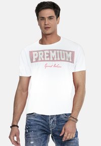 Weißes T-Shirt mit kurzen Ärmeln und rotem Text "PREMIUM" und "Good Wear", mit Rundhalsausschnitt, getragen mit blauen, ausgewaschenen Jeans.