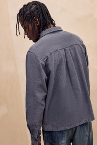 Button-up skjorte i marineblå og hvit rutete mønster, med lange ermer, en ryggfold, og kragehals. Jeans i denim synlige under.