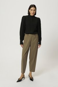 Blusa nera a pieghe, colletto alto, maniche lunghe a sbuffo abbinata a pantaloni a righe sottili marrone chiaro e scarpe a punta nere con tacco.