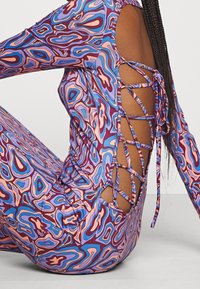 Dopasowana sukienka z długim rękawem w wielokolorowy abstrakcyjny wzór. Posiada wycięcie na plecach z wiązaniem. Gładki, elastyczny materiał.