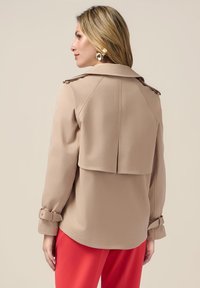Beige trenchcoat met een relaxte pasvorm, voorzien van een rugplooi en gebelte manchetten, textiele stof en een eenvoudig ontwerp van de kraag.