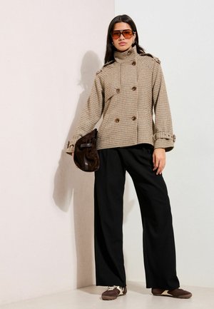 Brūns rūtainais dubultpogas žakete ar augstu apkakli, melnas platu kāju bikses un brūna soma. Stilizēts ar brūnām kurpēm un lielizmēra saulesbrillēm.