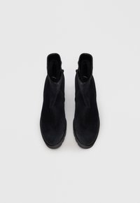 Bottines noires en daim avec une texture lisse, dotées de zips sur les côtés et d'un design à bout rond, sur un fond blanc uni.