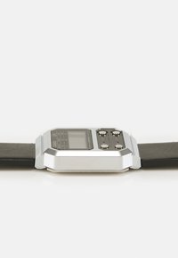 Montre numérique avec un cadran rectangulaire, boîtier en métal argenté et bracelet en cuir noir. Dotée de trois boutons et d'un affichage numérique.