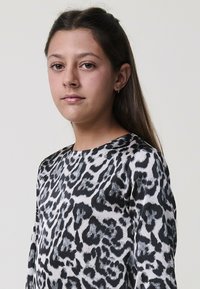 Gornji dio s leopard printom u crno-bijeloj boji, s glatkom, svilenom teksturom i okruglim izrezom. Dugi rukavi i opušteni kroj.