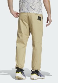 Beige joggerbyxor med elastiska mudd, rundade sömmar och en svart etikett på baksidan. I kombination med svarta och grå sportskor.