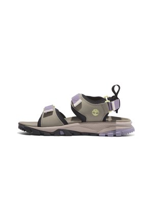 Sandalias deportivas con un upper sintético beige, acentos negros, correas ajustables y una suela de goma texturizada con detalles morados.