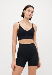 Crop top de sport noir avec fines bretelles et décolleté en V, associé à un short noir taille haute. Le tissu semble lisse et ajusté.