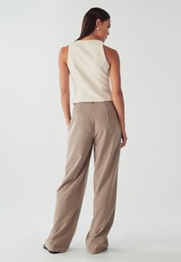 Top senza maniche di color crema con collo alto, abbinato a pantaloni beige a vestibilità ampia caratterizzati da una sottile texture e una fascia in vita piatta.