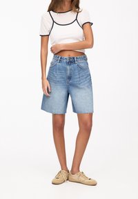 Jasnoniebieskie szorty jeansowe z postrzępionym wykończeniem, wysokim stanem i pięcioma kieszeniami. W zestawie z białym, krótkim T-shirtem z czarną lamówką.