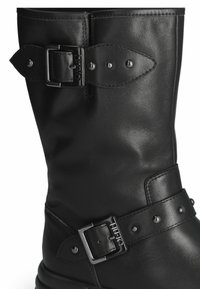 Stivale nero in pelle fino al ginocchio con cinturino regolabile e fibbia argentata, decorato con borchie metalliche e una texture liscia.