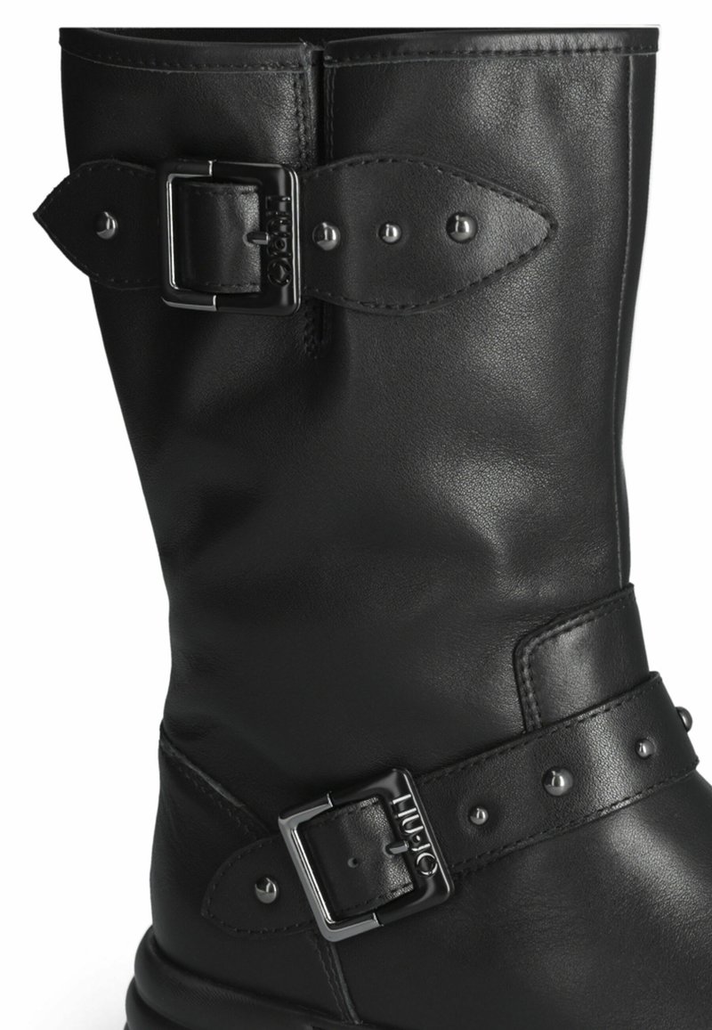 Schwarze Leder kniehohe Stiefel mit einem verstellbaren Riemen und einer silbernen Schnalle, akzentuiert mit Metallnieten und glatter Oberfläche.