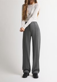 Haut gris clair à manches longues associé à un pantalon large gris taille haute. Le pantalon présente des plis et une finition lisse et texturée. Chaussures noires.