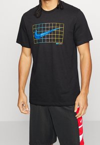 Camiseta de algodón negra con un logo azul de Nike Swoosh dentro de una rejilla, con acentos amarillos y azules y el texto "JUST DO IT" en la parte inferior.