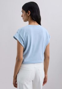 Camiseta de algodón azul claro con mangas enrolladas, escote redondo y corte relajado. Combinada con pantalones blancos de cintura alta.