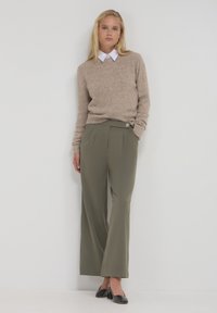 Maglione in misto lana beige con scollatura a manica corta, abbinato a pantaloni a gamba larga verde oliva con pieghe frontali e dettaglio decorativo a bottoni.