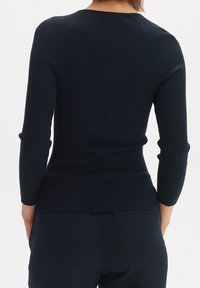 Marinblå ribbad långärmad topp med en figurnära passform, rund halslinning och textilstruktur. Bakifrån visas detaljer vid axelsömmarna.
